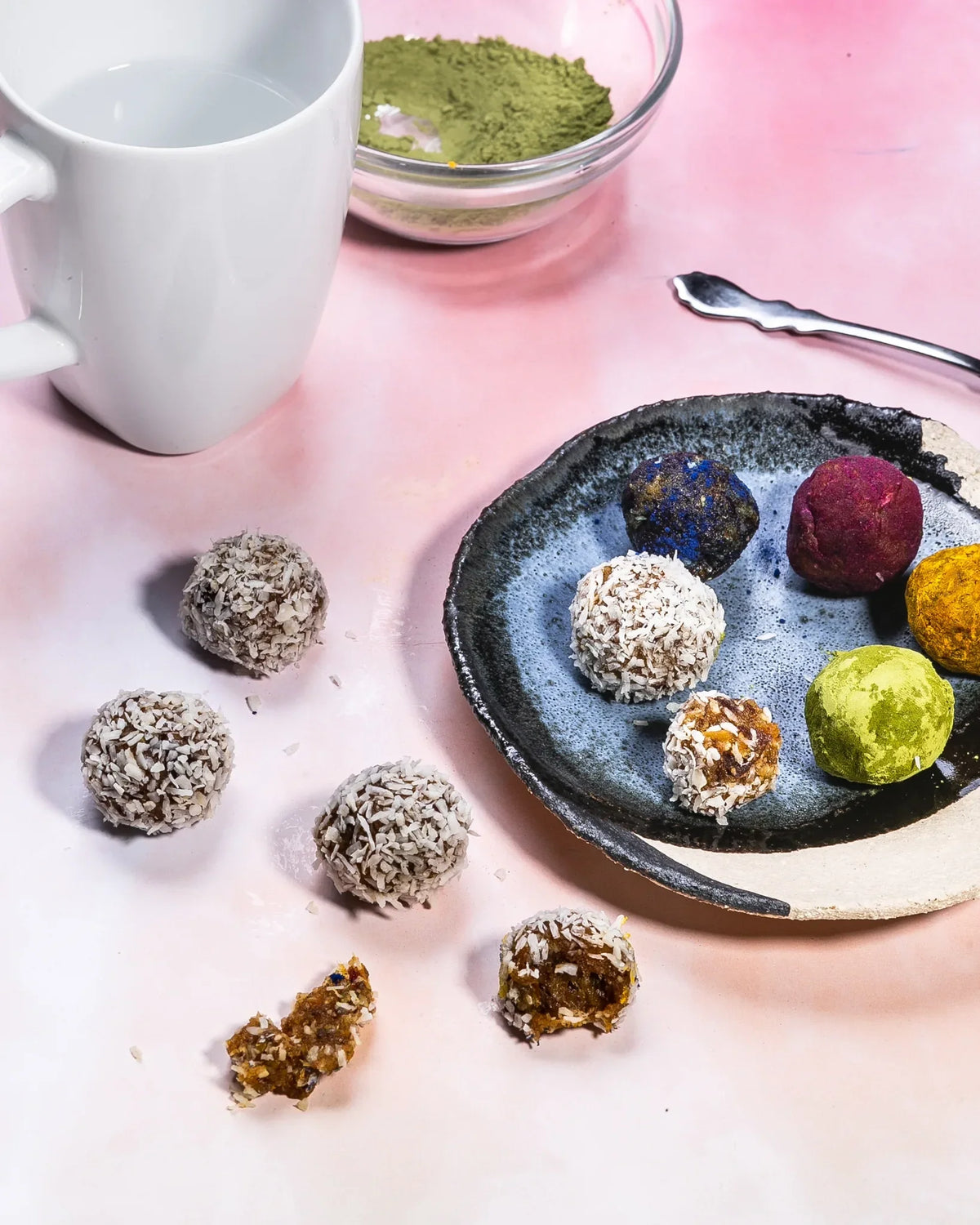 Matcha and beetroot energy balls and truffles on a ceramic plate with matcha powder and white mug.