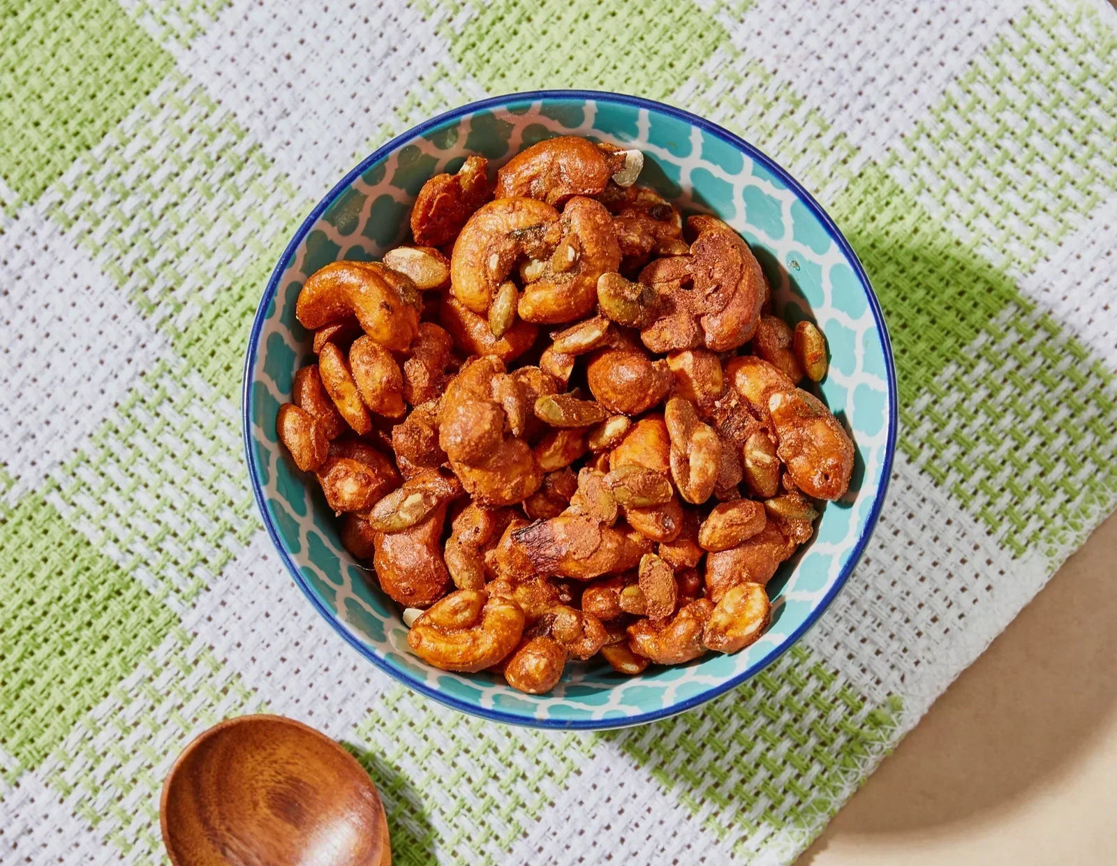 Amazin' Graze nut mix served in a patterned bowl on a green cloth beside a wooden spoon.