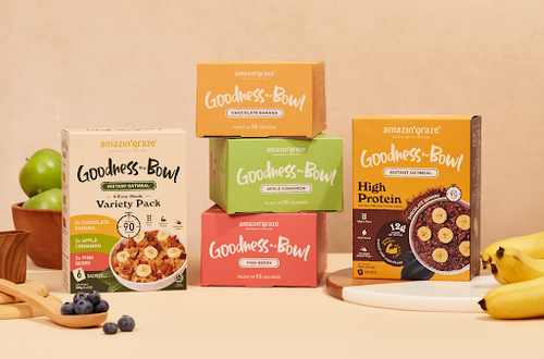 Amazin' Graze Goodness Bowl oatmeal boxes displayed with bananas, apples, blueberries, and serving bowls.